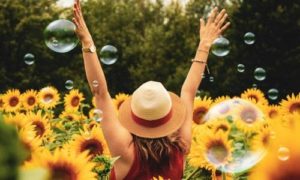 Mark Roemer image of a woman in a field of sunflowers and bubbles with her arms up in the air